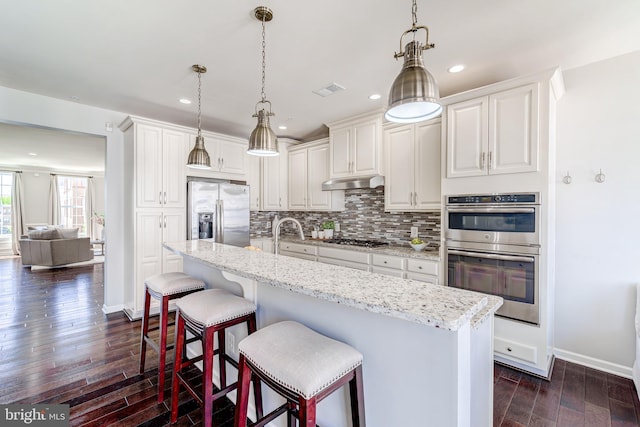 kitchen featuring decorative backsplash, white cabinets, dark wood-style floors, under cabinet range hood, and stainless steel appliances
