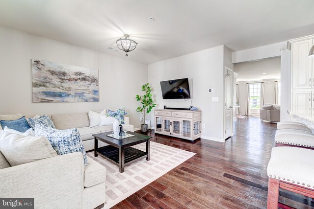 living room featuring visible vents, baseboards, wood finished floors, and an inviting chandelier