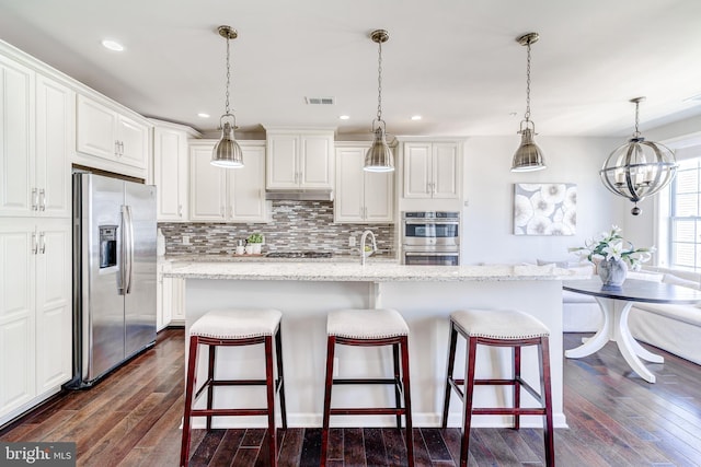 kitchen with under cabinet range hood, stainless steel appliances, backsplash, visible vents, and dark wood-style floors