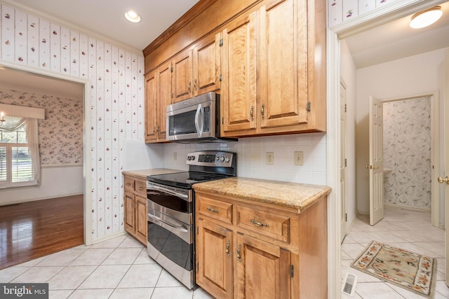 kitchen featuring appliances with stainless steel finishes, tasteful backsplash, wallpapered walls, and light tile patterned floors