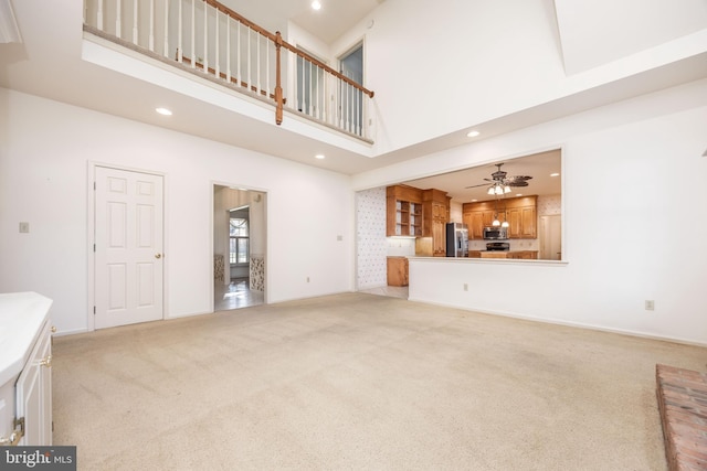 unfurnished living room with ceiling fan, light carpet, a towering ceiling, baseboards, and recessed lighting