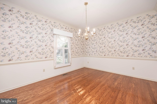 empty room with wallpapered walls, wood finished floors, visible vents, wainscoting, and a chandelier