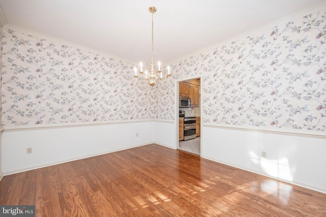 unfurnished dining area with wallpapered walls, a chandelier, a wainscoted wall, light wood finished floors, and ornamental molding