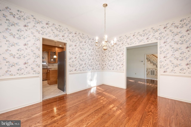 unfurnished dining area featuring wallpapered walls, a wainscoted wall, wood finished floors, and a notable chandelier
