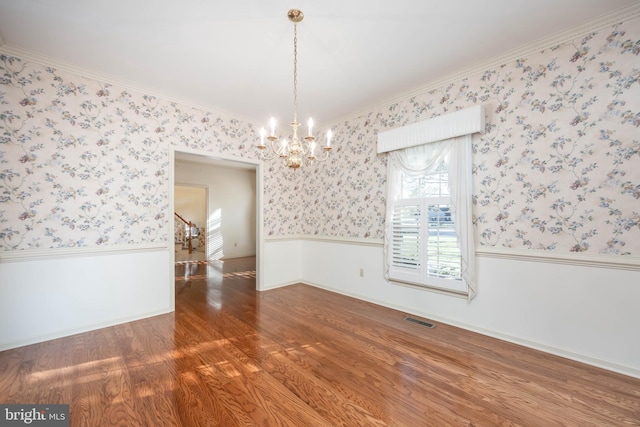 unfurnished dining area featuring wood finished floors, wallpapered walls, wainscoting, an inviting chandelier, and visible vents