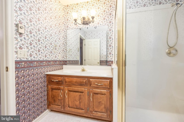 full bath with an inviting chandelier, vanity, wallpapered walls, and a stall shower