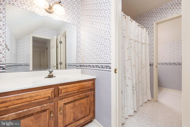 full bath with wallpapered walls, vaulted ceiling, tile patterned flooring, and vanity