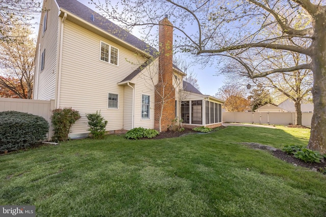 back of house featuring a yard, a sunroom, a fenced backyard, and a chimney