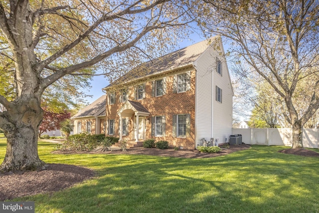 colonial-style house with brick siding, fence, central AC, and a front yard
