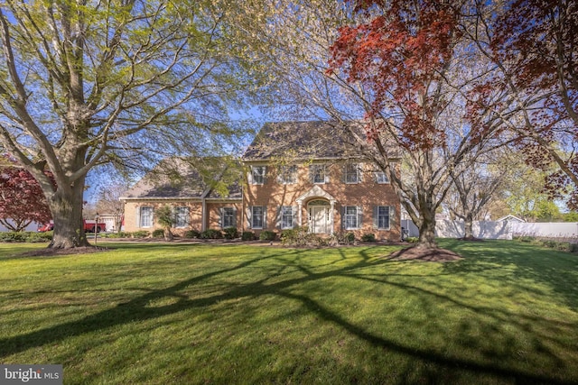 colonial-style house with fence, a front lawn, and brick siding