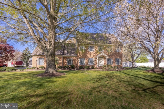 colonial home featuring brick siding, a front lawn, and fence