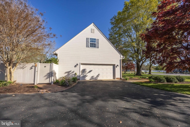 view of property exterior with a gate, an attached garage, aphalt driveway, and fence