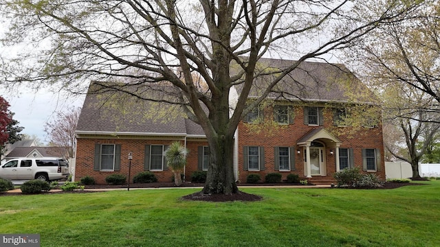 colonial house with brick siding, a front yard, and fence