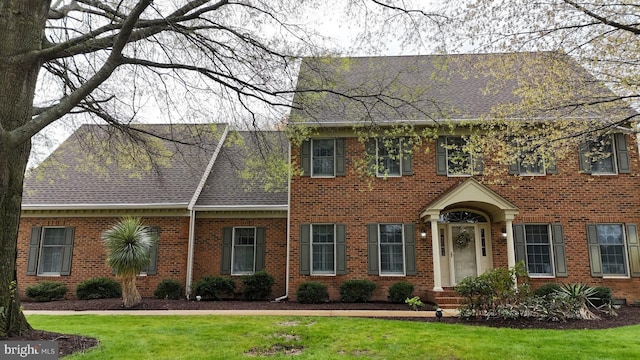 view of front of home with a front lawn, brick siding, and a shingled roof