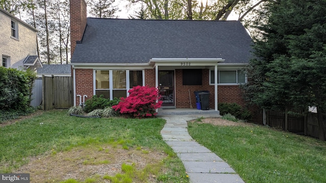 view of front of home with brick siding, fence, a chimney, and a front lawn
