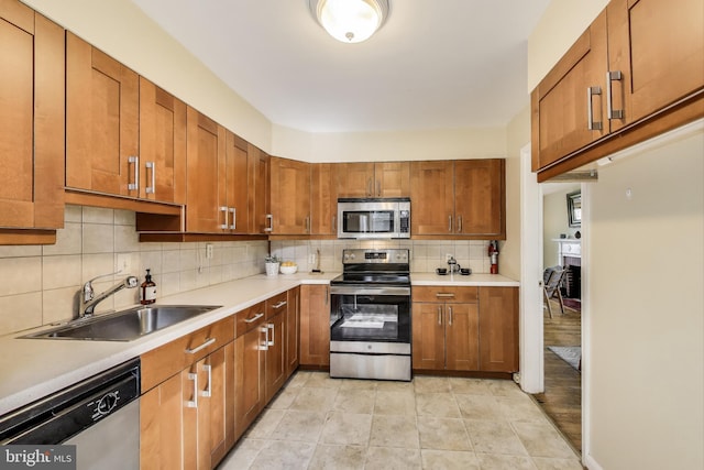 kitchen featuring brown cabinetry, light countertops, tasteful backsplash, a sink, and appliances with stainless steel finishes
