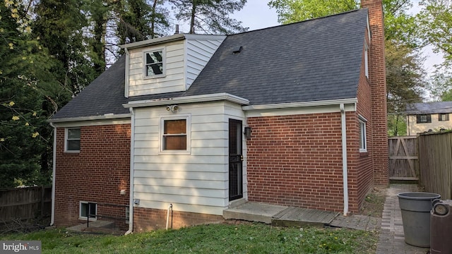 back of property with brick siding, fence, a chimney, and roof with shingles