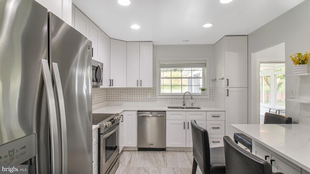kitchen with backsplash, appliances with stainless steel finishes, light stone countertops, a sink, and marble finish floor