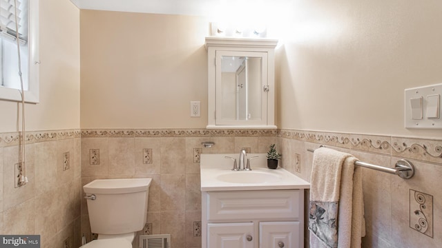 bathroom with visible vents, vanity, wainscoting, toilet, and tile walls