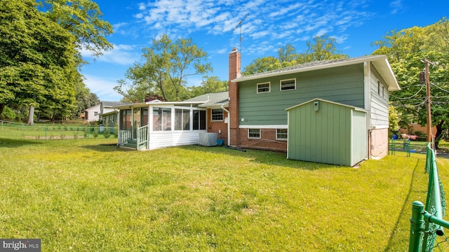 rear view of property with a storage shed, a lawn, a chimney, and a sunroom
