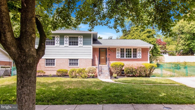 split level home with brick siding, a front lawn, and fence