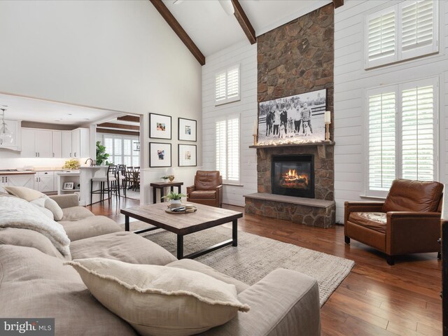 living room featuring beam ceiling, high vaulted ceiling, wood-type flooring, and a stone fireplace