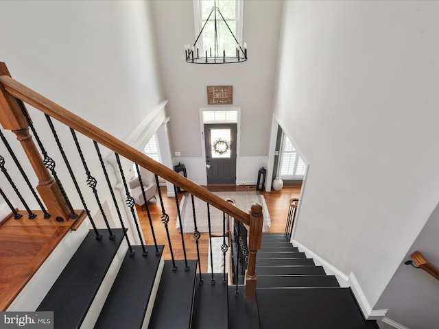 stairs with a towering ceiling, wood finished floors, and a healthy amount of sunlight