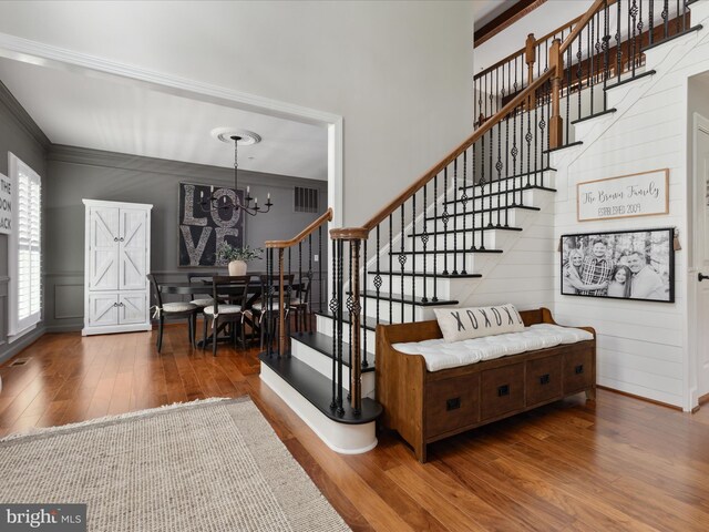 stairs with crown molding, an inviting chandelier, a decorative wall, wood finished floors, and visible vents