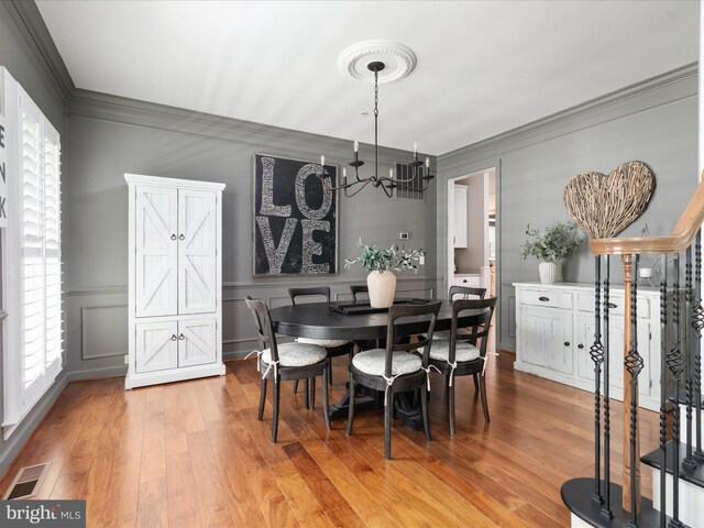 dining space featuring visible vents, crown molding, light wood-type flooring, an inviting chandelier, and a decorative wall