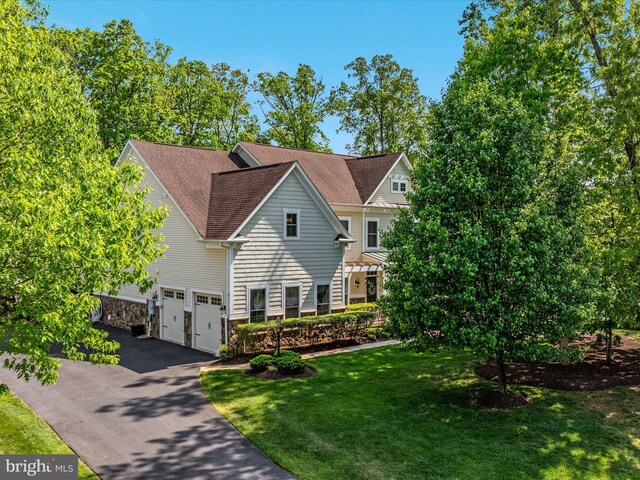 view of front facade featuring driveway, a front yard, a garage, a shingled roof, and stone siding