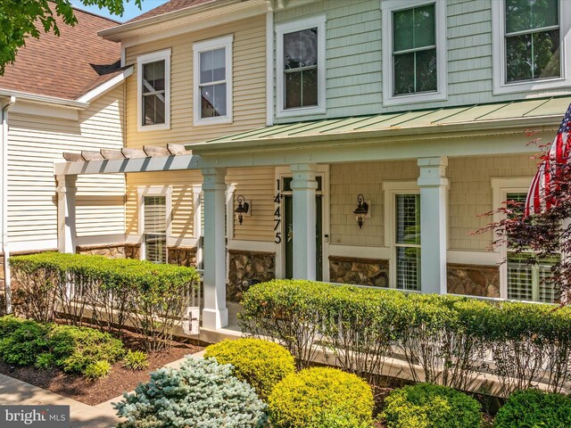 view of front of property featuring covered porch, a pergola, stone siding, a standing seam roof, and metal roof