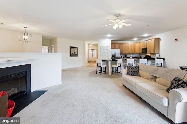 living area featuring ceiling fan with notable chandelier, light colored carpet, and a fireplace with flush hearth