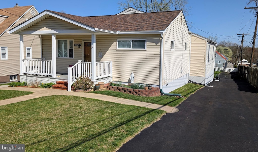 bungalow-style home featuring fence, a shingled roof, a front lawn, driveway, and covered porch