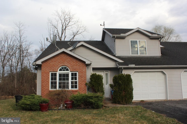 view of front of house with a front lawn, roof with shingles, an attached garage, driveway, and brick siding