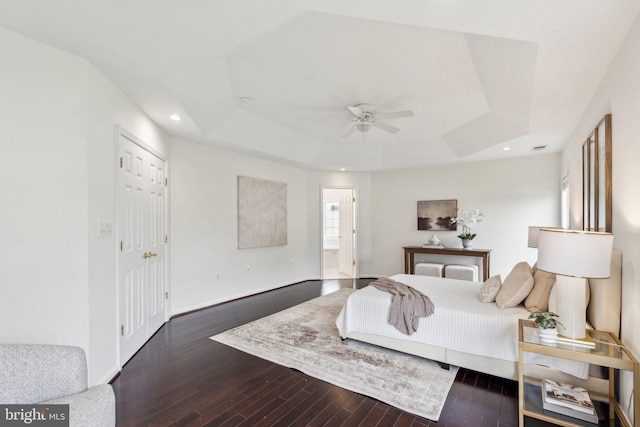 bedroom featuring wood finished floors, connected bathroom, a tray ceiling, baseboards, and recessed lighting