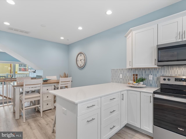 kitchen featuring light wood finished floors, stainless steel appliances, visible vents, white cabinetry, and decorative backsplash