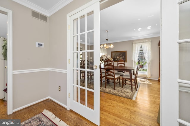 doorway to outside featuring wood finished floors, visible vents, crown molding, and a notable chandelier