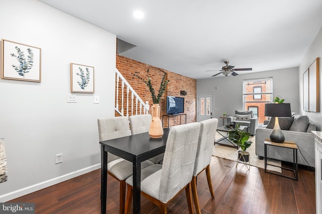 dining space with dark wood finished floors, a ceiling fan, baseboards, stairs, and brick wall