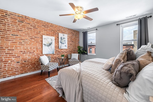 bedroom with visible vents, baseboards, brick wall, a ceiling fan, and wood finished floors