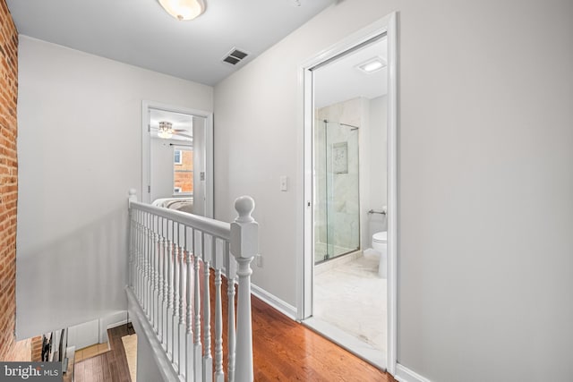 corridor featuring baseboards, wood finished floors, visible vents, and an upstairs landing