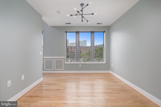 empty room with baseboards, a notable chandelier, light wood finished floors, and visible vents