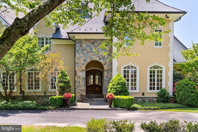 exterior space featuring stone siding, a high end roof, stucco siding, and french doors