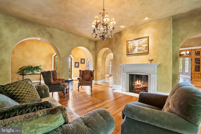living room featuring a notable chandelier, recessed lighting, a glass covered fireplace, wood finished floors, and arched walkways