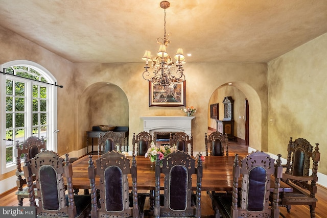 dining space with arched walkways, a notable chandelier, baseboards, and wood finished floors