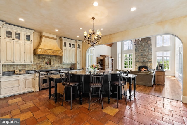 kitchen featuring a center island, high end stainless steel range oven, an inviting chandelier, custom range hood, and cream cabinets