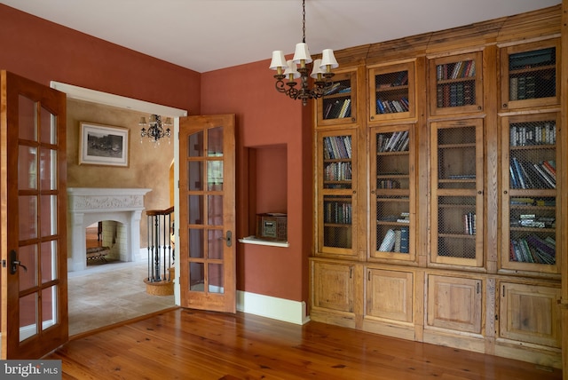 unfurnished dining area featuring an inviting chandelier, french doors, and wood finished floors