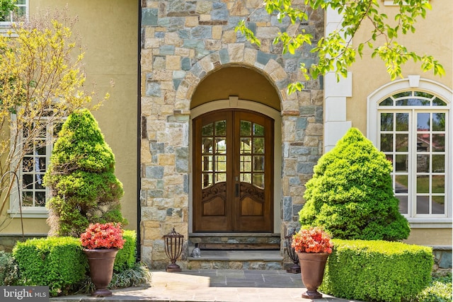 view of exterior entry featuring stone siding, stucco siding, and french doors