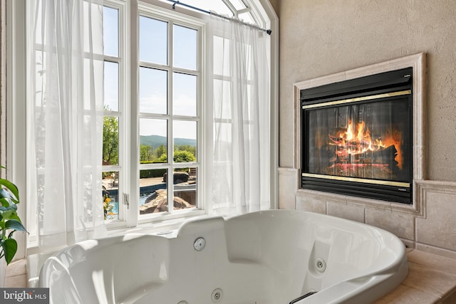full bath with a whirlpool tub, a textured wall, and a glass covered fireplace