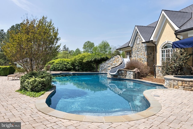 view of pool featuring a pool with connected hot tub, a patio, and a water slide