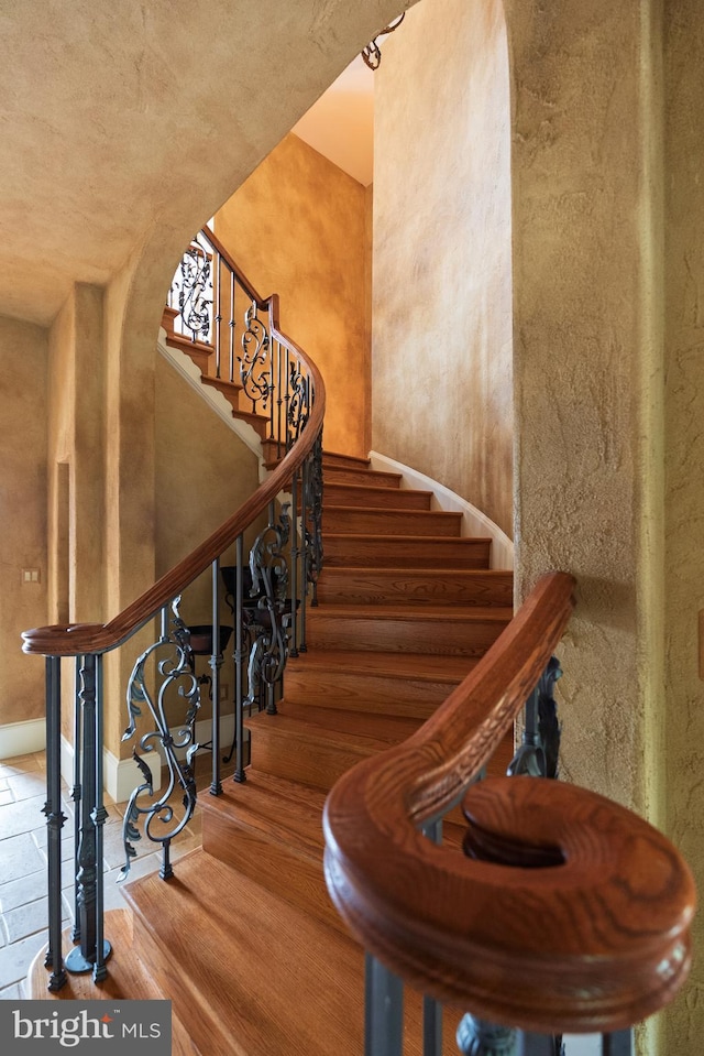 staircase with arched walkways and wood finished floors